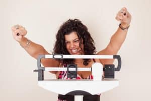 Woman celebrating weight loss success on scale, expressing joy and motivation for a renewed weight loss journey.