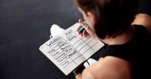 Person writing in a notebook with a workout plan, emphasizing personal fitness routine and accountability in weight loss efforts.