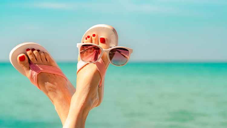 Feet in pink flip-flops resting on the beach with sunglasses, symbolizing relaxation and enjoyment during vacation while maintaining weight loss goals.
